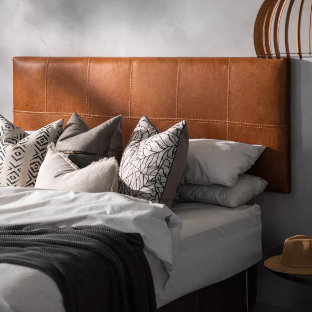 Patterned white, brown, & black pillows on the bed with white linen, and a dark tan leather headboard - Moroccan Interior.