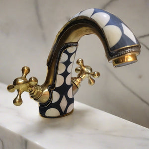 Brass Bathroom Faucet with dual handles standing on a countertop with a marbel background 
