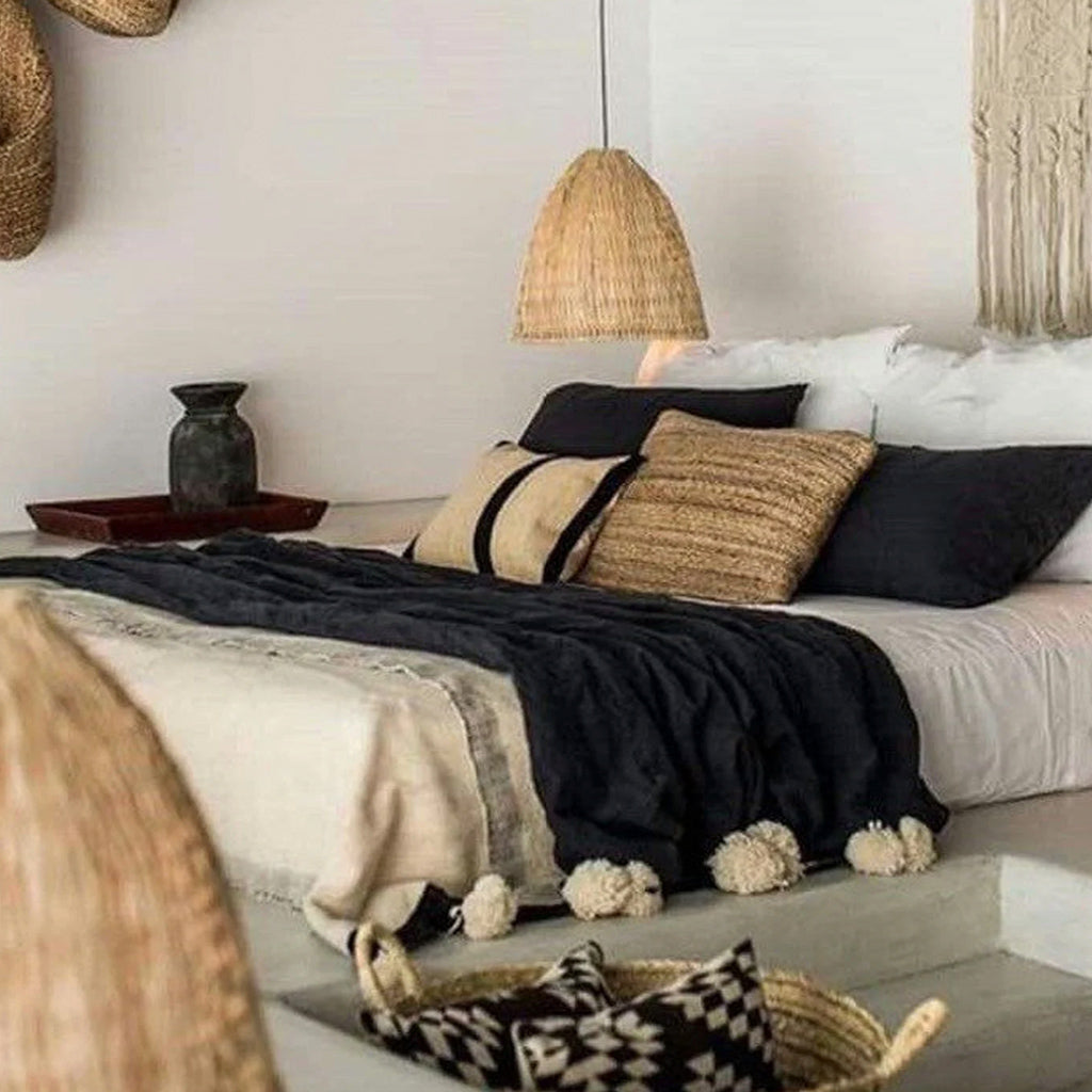 Black Moroccan Pom pom blanket on top of a bed with pillows in a bedroom with berber furniture - Moroccan Interior