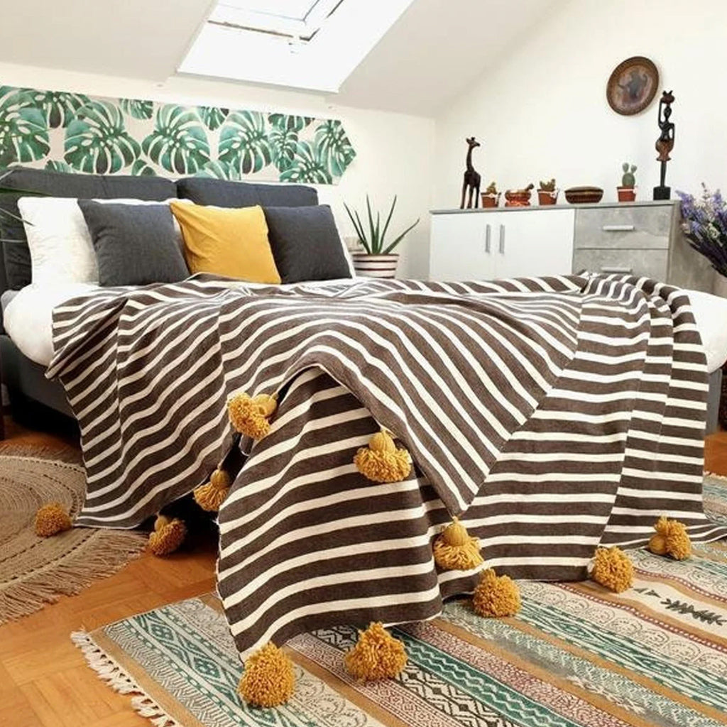 Gray and white Moroccan Pom pom blanket on top of a bed with pillows in a bedroom with furniture - Moroccan Interior