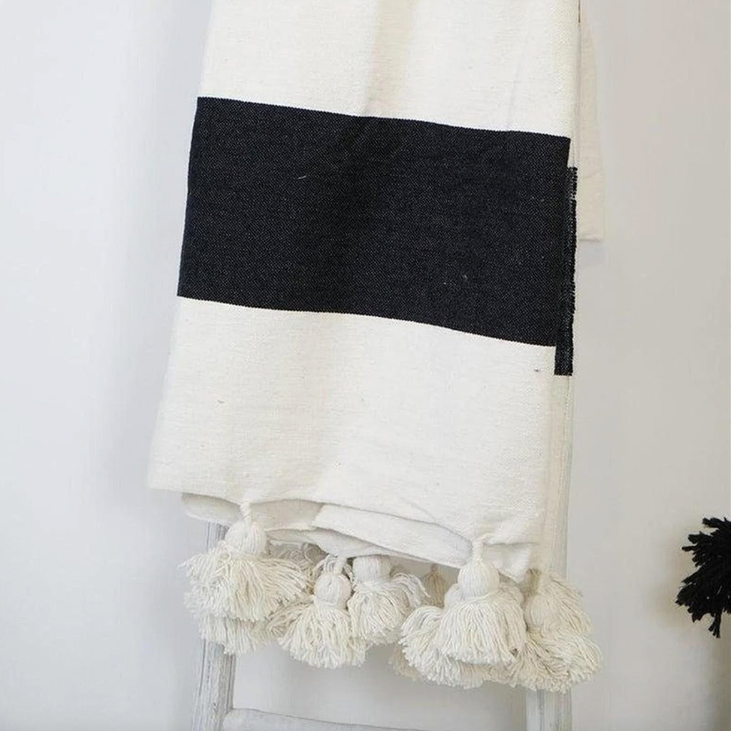 Moroccan Pompom Blanket in white and black draped over a wooden ladder - Moroccan Interior