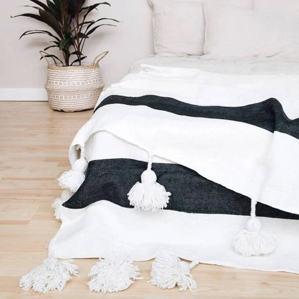 White and black Moroccan Pom pom blanket on top of a bed with pillows in a bedroom with berber furniture - Moroccan Interior