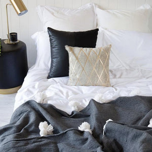 Dark gray Moroccan Pom pom blanket on top of a bed with pillows in a bedroom with furniture - Moroccan Interior