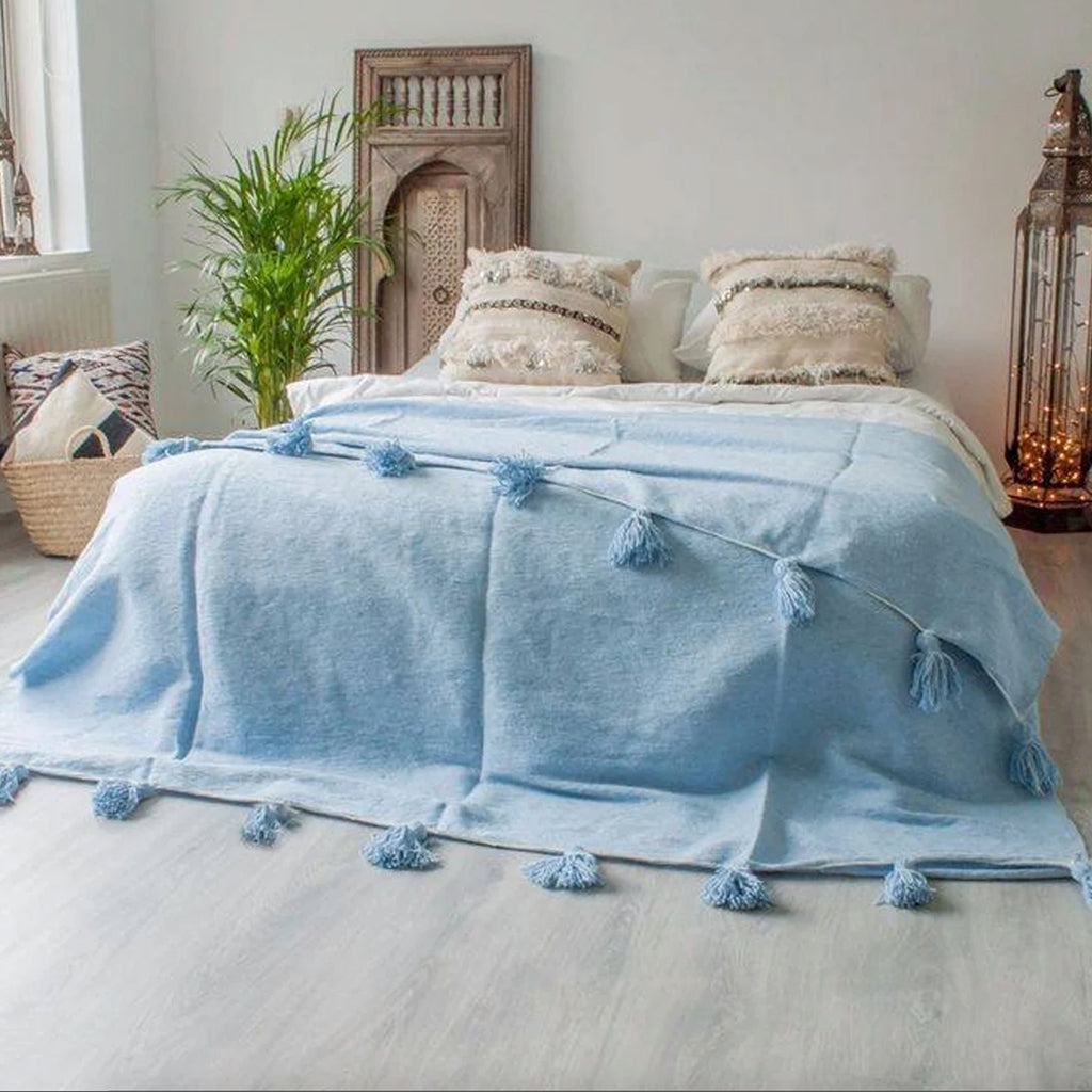 Light blue Moroccan Pom pom blanket on top of a bed with pillows in a bedroom with berber furniture - Moroccan Interior