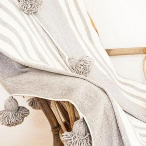 Moroccan Pompom Blanket in white and gray laid on top of a wood chair - Moroccan Interior