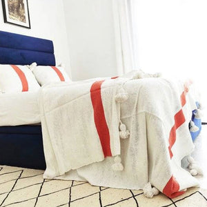 White  and orange Moroccan Pom pom blanket on top of a bed with pillows in a bedroom with furniture - Moroccan Interior