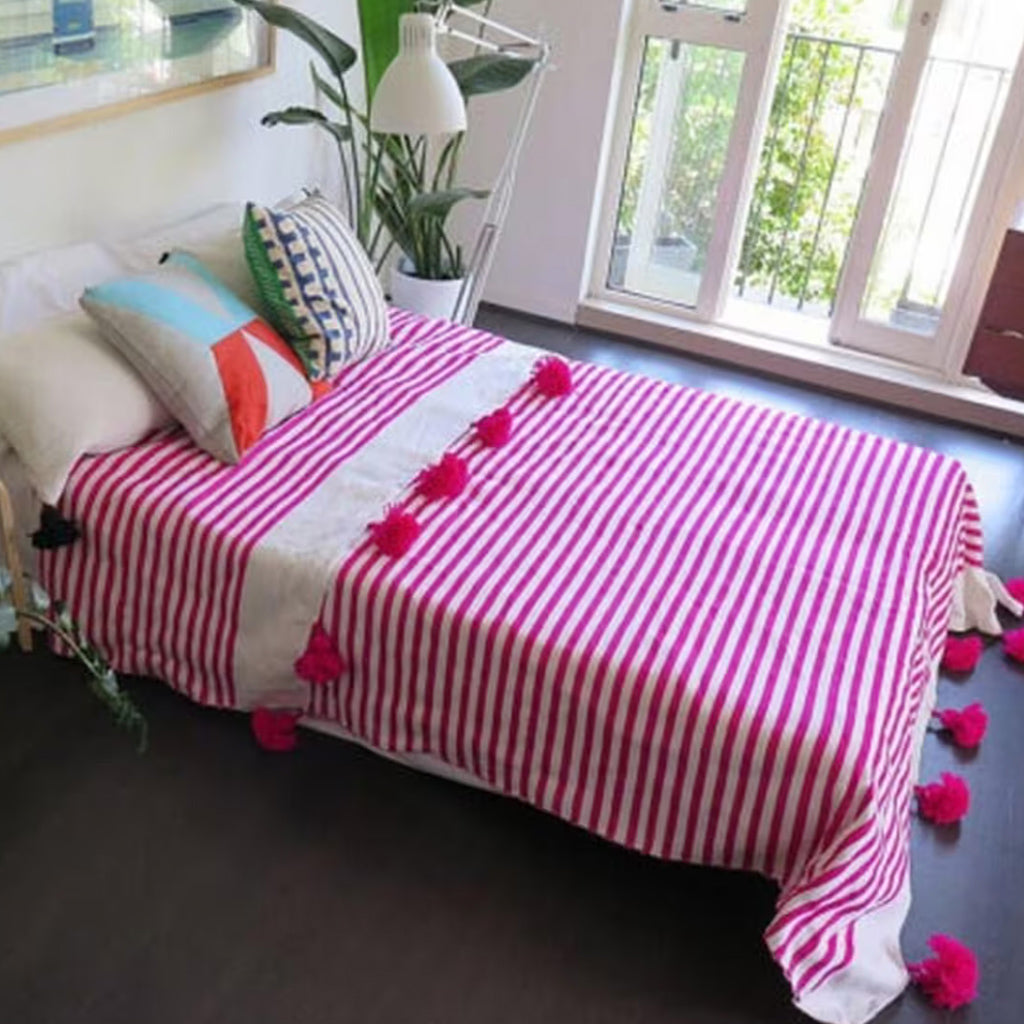 Pink and white Moroccan Pom pom blanket on top of a bed with pillows in a bedroom with big window - Moroccan Interior