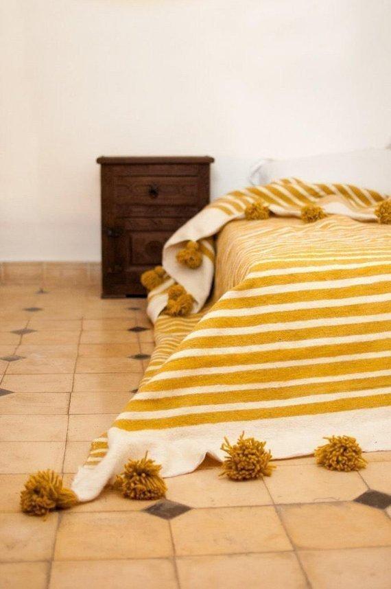 White and yellow Moroccan Pom pom blanket on top of a bed with pillows in a bedroom with furniture - Moroccan Interior