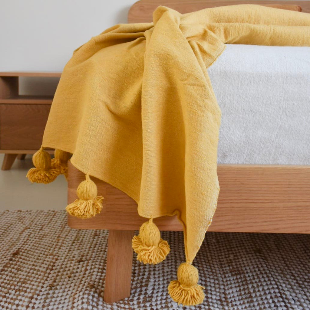 Yellow Moroccan Pom pom blanket on top of a bed  in a bedroom with furniture - Moroccan Interior