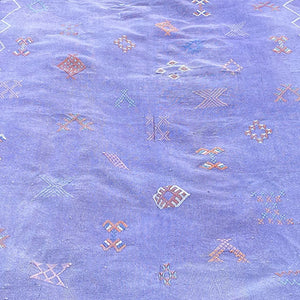 Close-up of a Moroccan sabra cactus silk rug in lavender purple, showcasing intricate handwoven tribal embroidery in multicolor geometric motifs