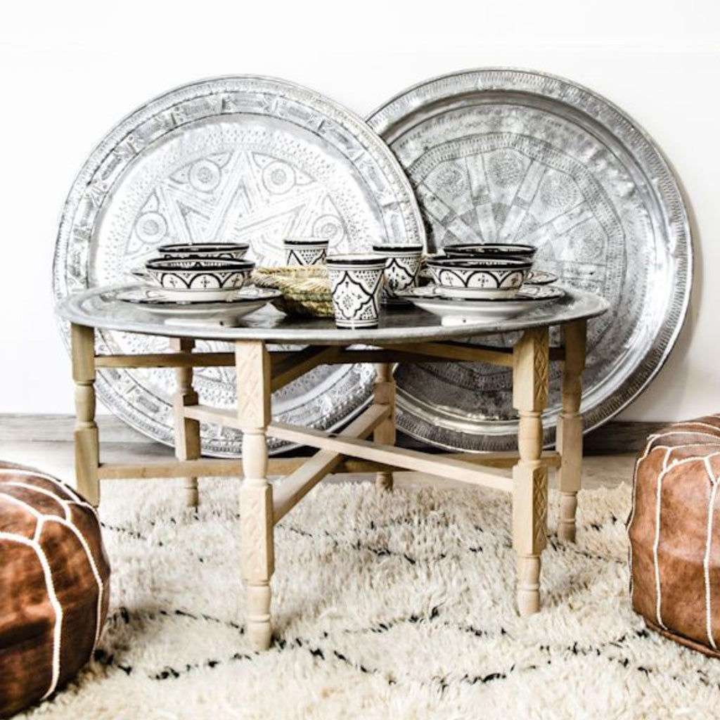 A stunning Moroccan tea table featuring a hand-engraved aluminum tray resting on natural cedarwood folding legs, perfect for adding an exotic touch to any home decor.