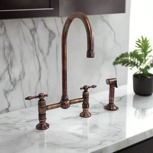 Antique copper kitchen bridge faucet with tall gooseneck spout and separate side sprayer on marble countertop