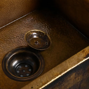 Close-up view of an antique copper sink showing a hammered texture and a dark bronze drain with a matching removable strainer