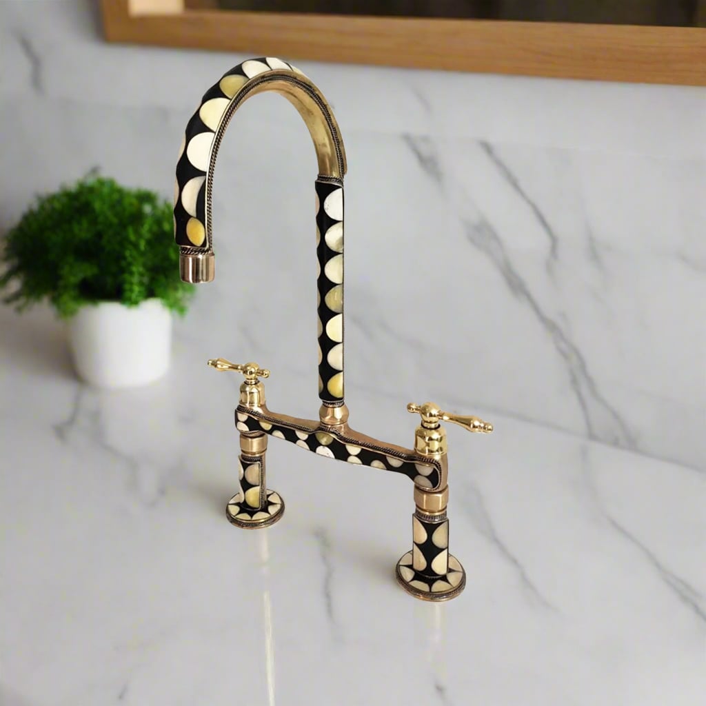 Art Deco-style bridge kitchen faucet with black and white circular inlay pattern and brass finish, set on a white marble countertop