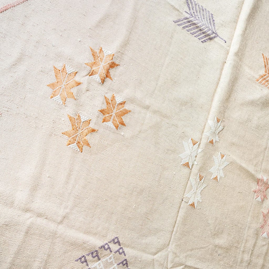 Close-up of beige Moroccan cactus silk rug showing embroidered floral motifs in orange and white with arrow detail