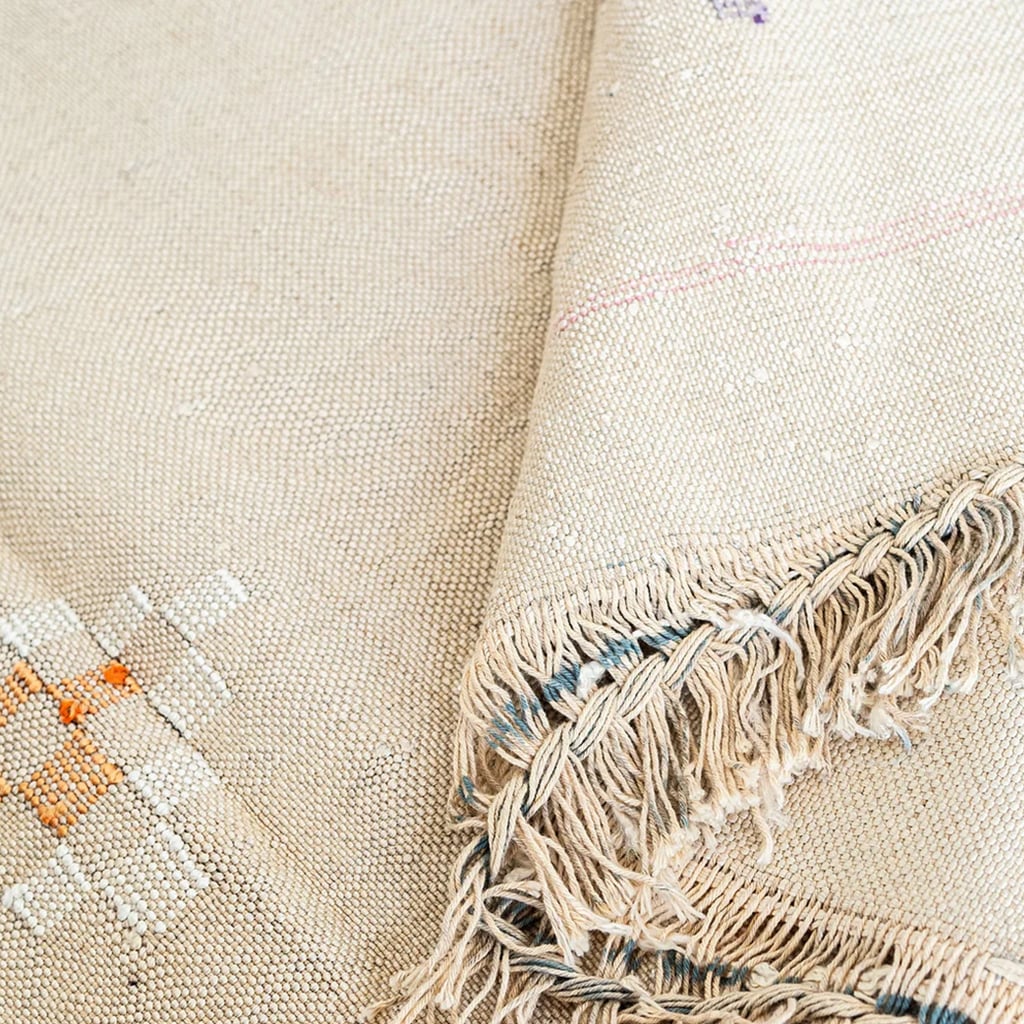 Corner of beige Moroccan cactus silk rug with knotted fringe and geometric embroidery in orange and cream