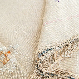 Corner of beige Moroccan cactus silk rug with knotted fringe and geometric embroidery in orange and cream