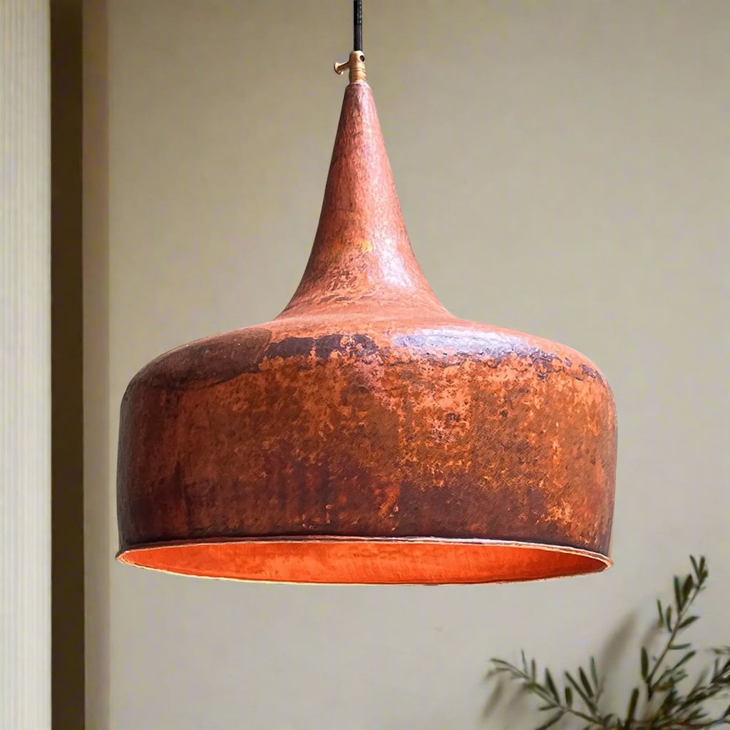 Close-up of bell-shaped hammered copper pendant light with a warm rustic patina, suspended against a soft neutral background