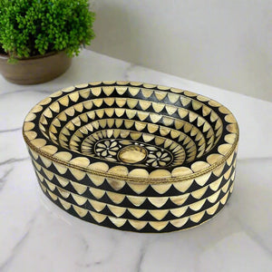 Oval decorative bathroom sink with intricate black and bone inlay pattern on marble countertop