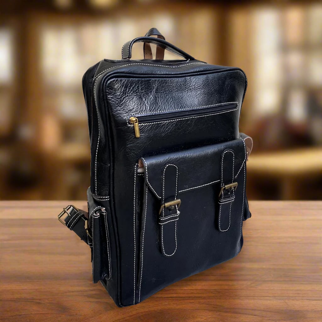 Angled view of a black leather backpack showcasing front buckle details, a spacious design, and white-stitched edges, resting on a polished table