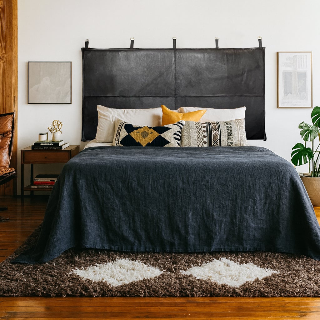 Bedroom with a black leather headboard, layered pillows, navy bedspread, and modern-boho decor in a cozy, natural-toned setting