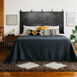 Bedroom with a black leather headboard, layered pillows, navy bedspread, and modern-boho decor in a cozy, natural-toned setting