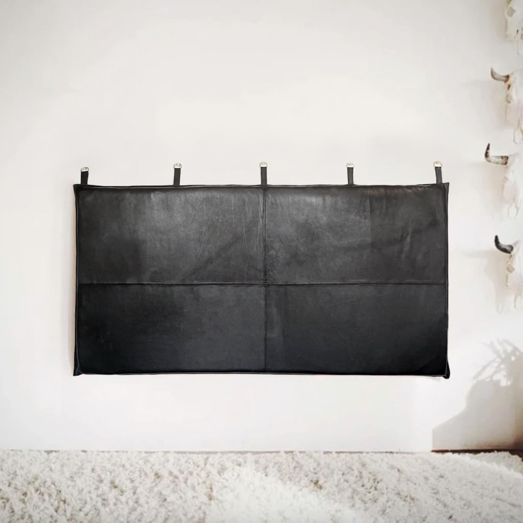 Black leather headboard with stitched panels and hanging loops, mounted on a white wall above a plush cream rug