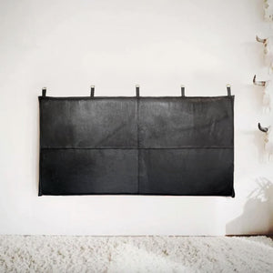 Black leather headboard with stitched panels and hanging loops, mounted on a white wall above a plush cream rug