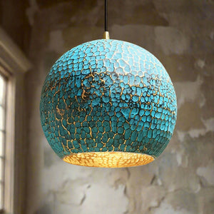 Globe-shaped hammered brass pendant with a vivid blue patina finish and golden interior, creating a striking focal point in a rustic room