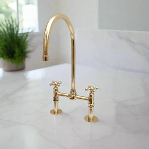 Classic brass bridge kitchen faucet with high arc gooseneck spout and cross handles, set on a marble countertop