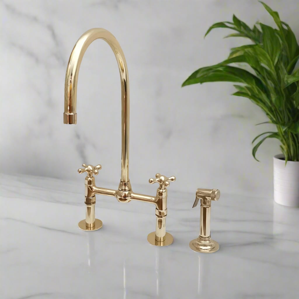 Elegant brass bridge kitchen faucet with a tall gooseneck spout and matching side spray installed on a marble countertop