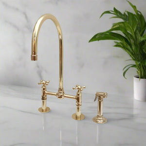 Elegant brass bridge kitchen faucet with a tall gooseneck spout and matching side spray installed on a marble countertop