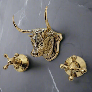 Wall-mounted brass faucet set with a sculpted bull head spout and cross handles on a dark marble wall