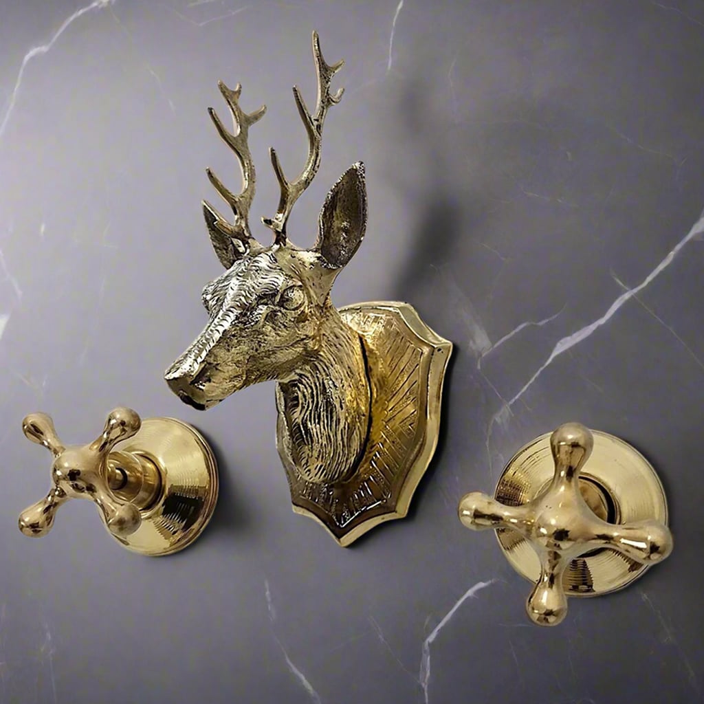 Wall-mounted brass faucet set with a sculpted deer head spout and cross handles on a dark marble wall