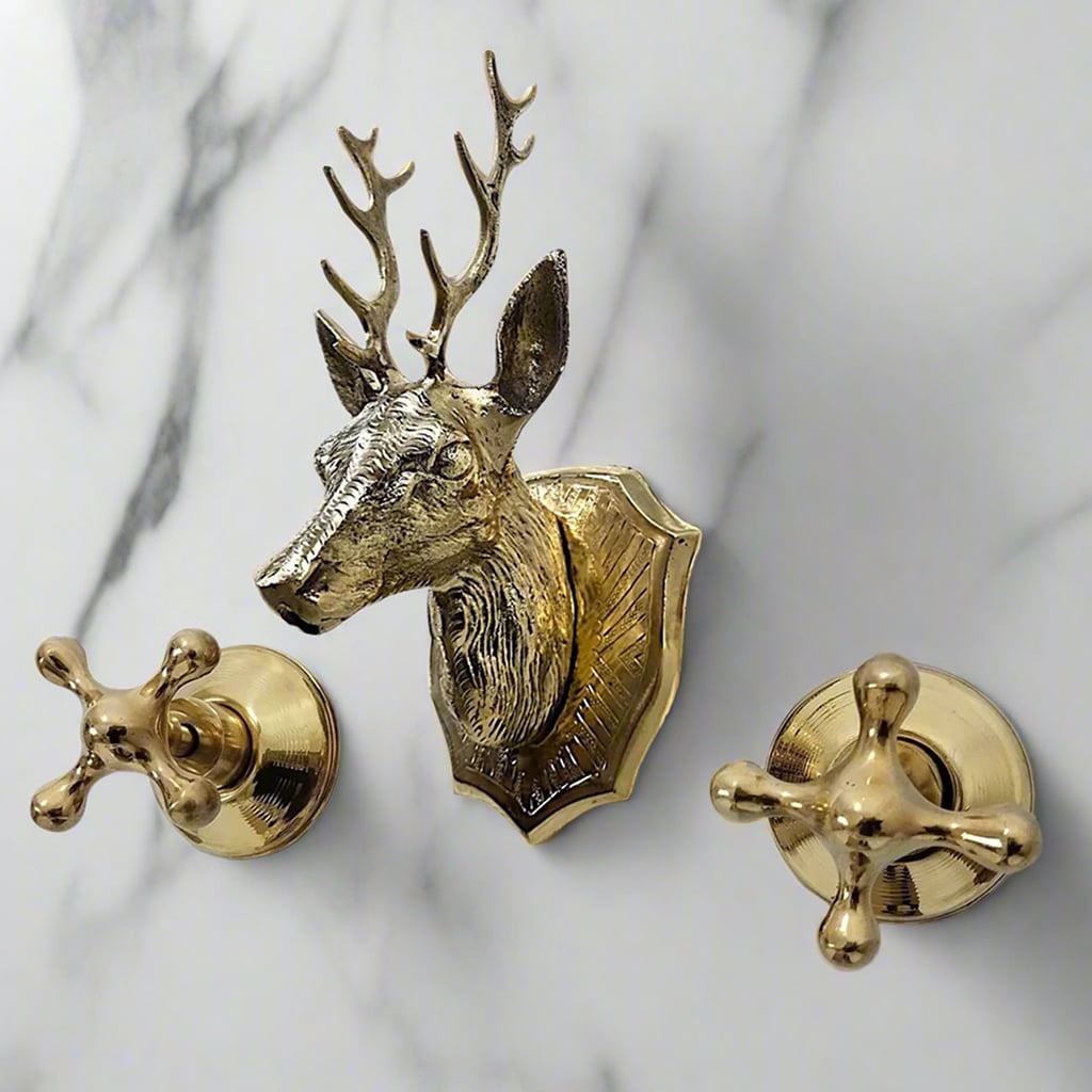 Decorative brass faucet with a deer head spout and cross handles mounted on white marble background