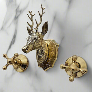 Decorative brass faucet with a deer head spout and cross handles mounted on white marble background