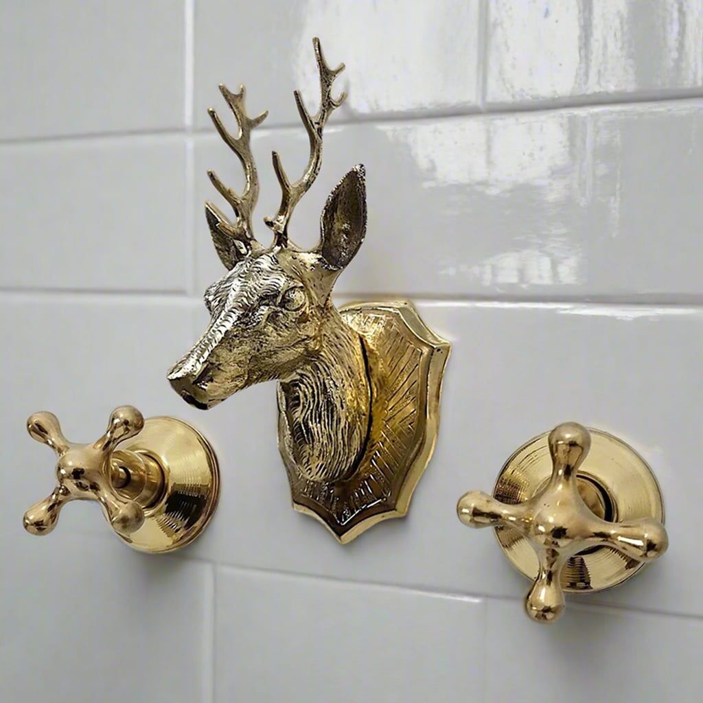 Close-up of a brass deer head faucet with matching cross handles mounted on glossy white tiled wall