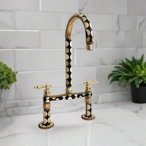 Brass kitchen faucet with geometric black and white inlay design and lever handles, mounted on a marble surface near subway tile backsplash