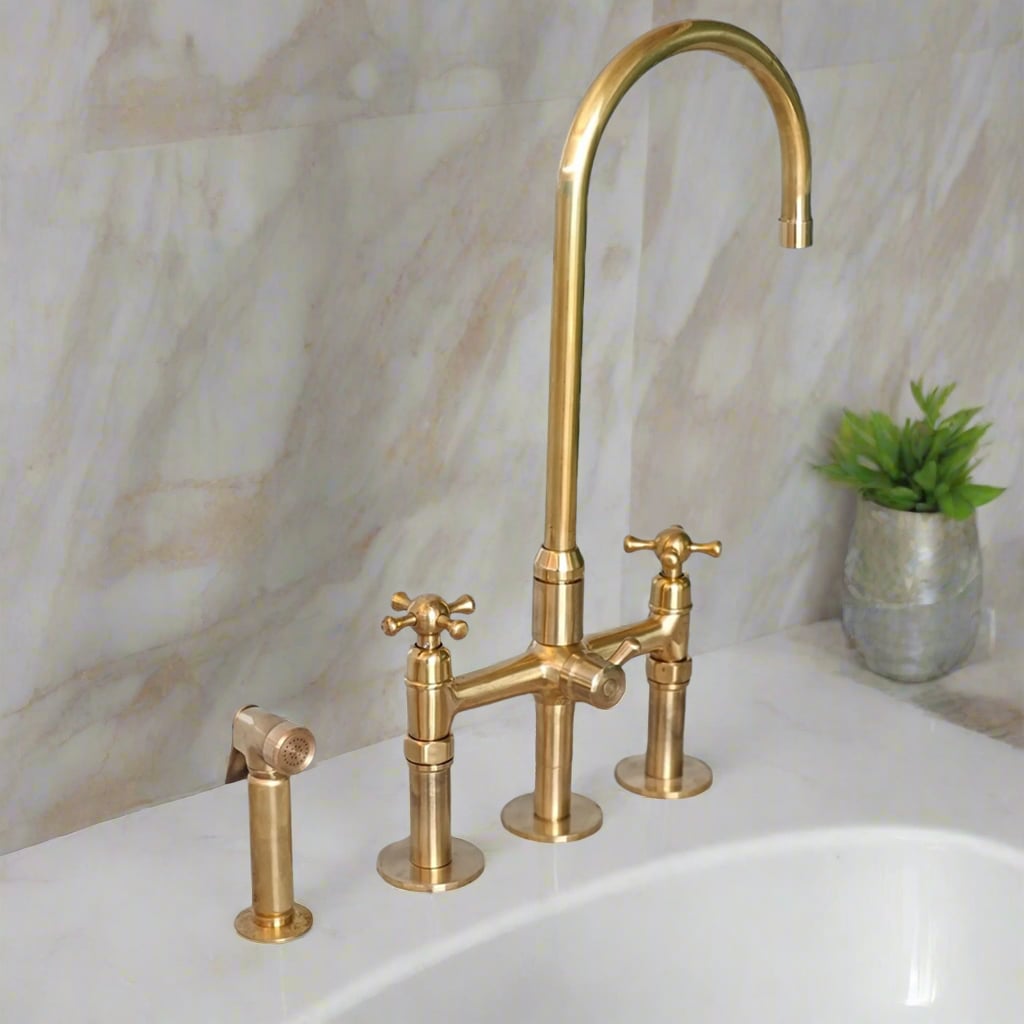 Vintage-style brass kitchen faucet with dual handles and side sprayer, mounted on creamy marble countertop with light veining and decorative vase