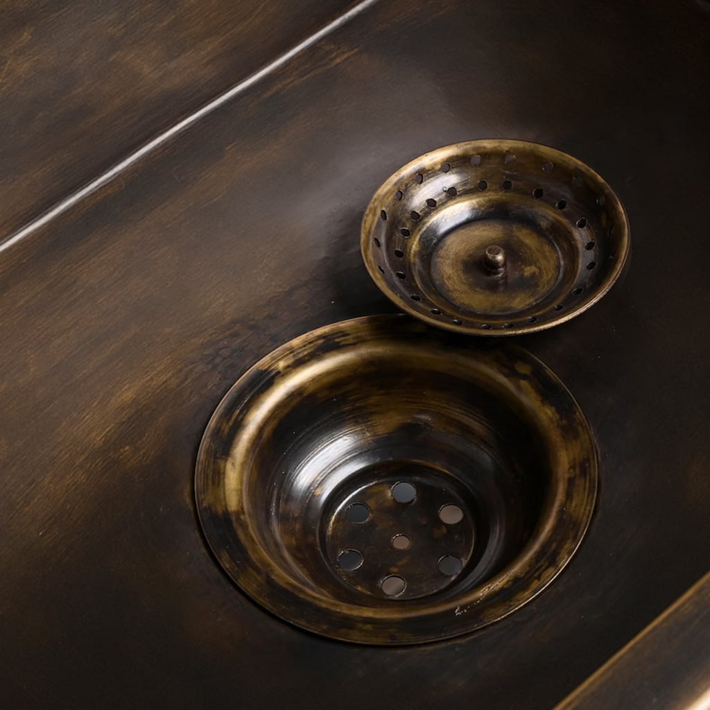 Close-up view of a brass sink drain with a removable strainer in a dark antique finish