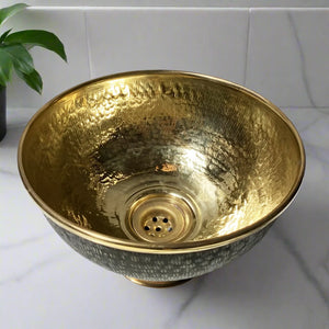 Top view of a handcrafted brass vessel sink with shiny gold interior and black etched outer surface, displayed on a marble vanity