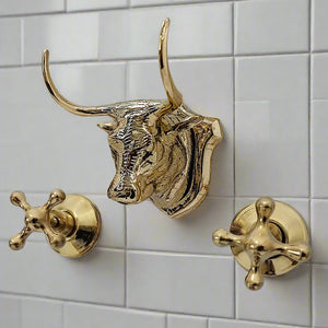 Close-up of a decorative brass bull head wall-mounted faucet with two cross handles, installed on white tiled bathroom wall