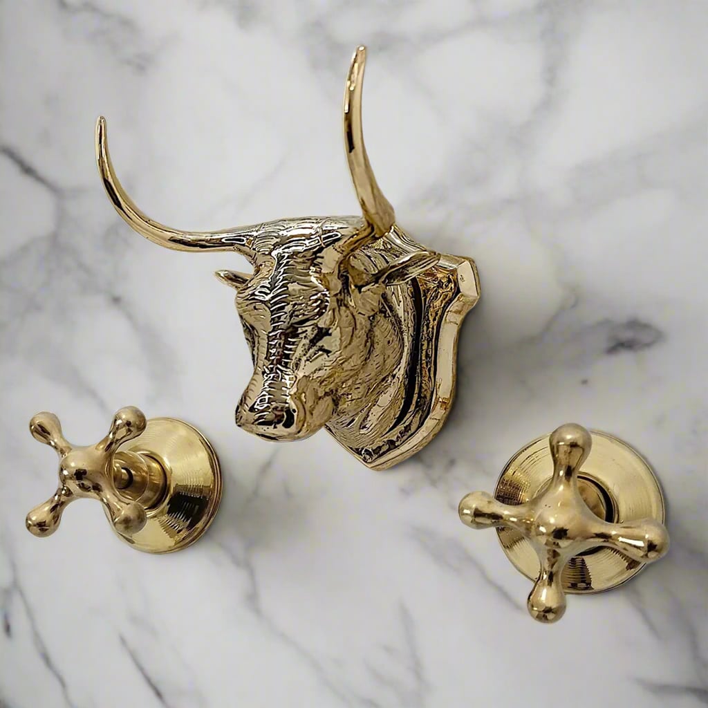 Decorative brass wall-mounted faucet set featuring a sculpted bull head spout and vintage-style cross handles, mounted on a marble tile wall