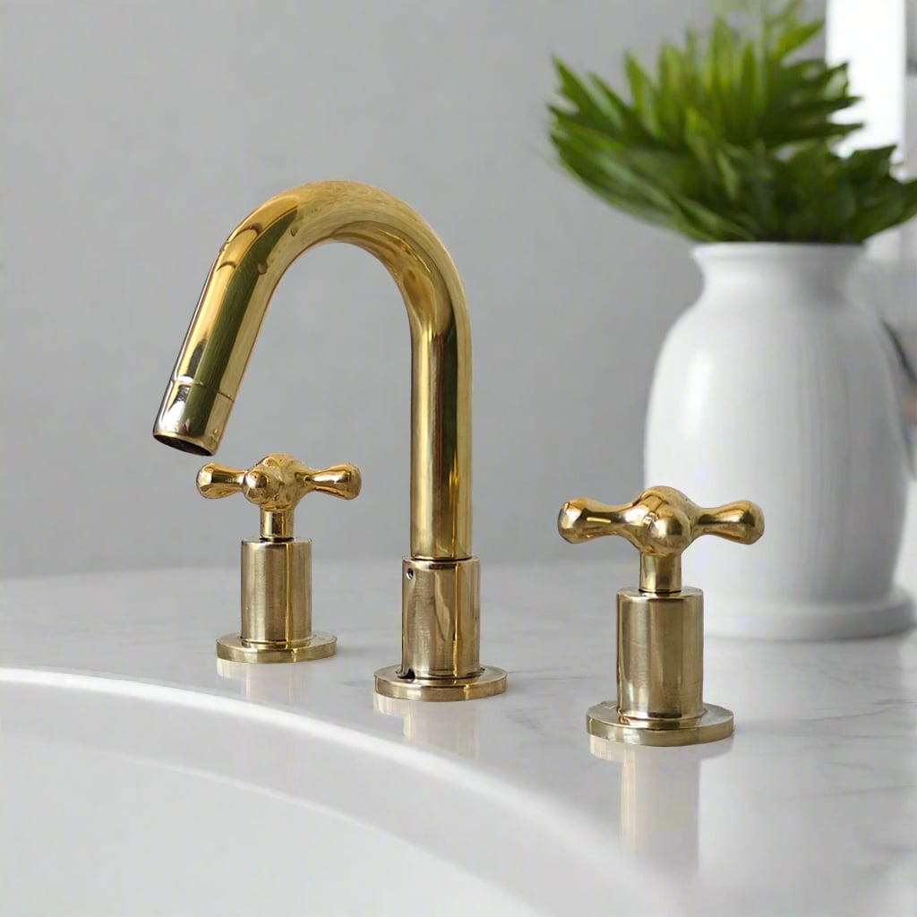 Polished brass widespread bathroom faucet with cross handles and arched spout, set on a clean white marble vanity surface