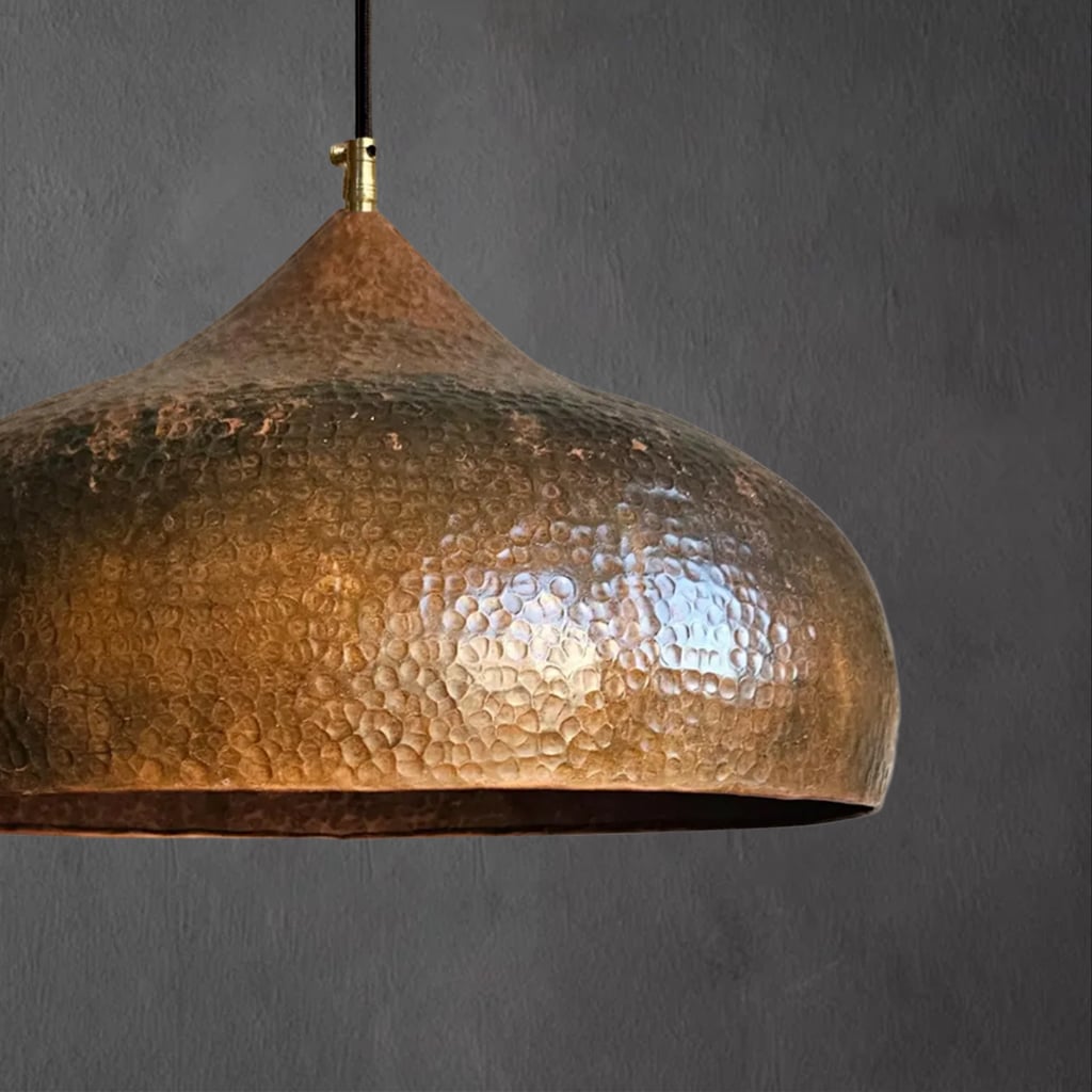 Close-up side view of a hammered copper pendant lamp, showcasing its dome form and artisanal hammered finish under ambient light