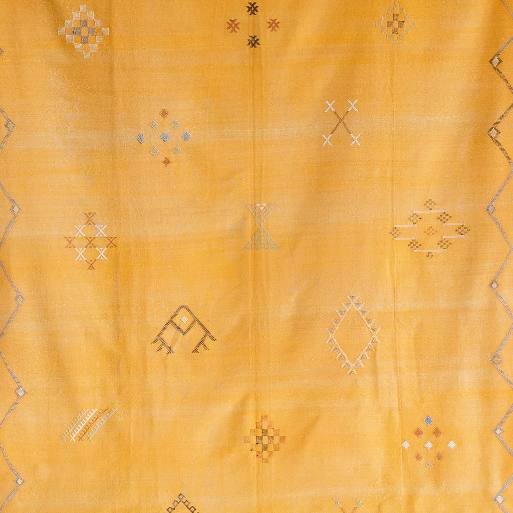 Close-up of mustard yellow Moroccan rug showing intricate handwoven Berber motifs in white, gray, and muted earth tones on a textured wool base