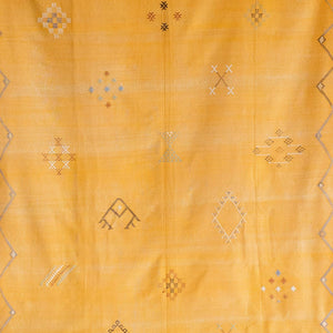 Close-up of mustard yellow Moroccan rug showing intricate handwoven Berber motifs in white, gray, and muted earth tones on a textured wool base