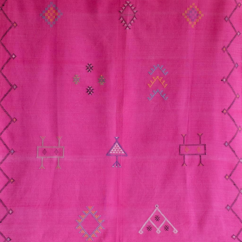 Close-up of a vibrant pink Moroccan rug featuring multicolored Berber symbols and geometric patterns, with a detailed handwoven texture