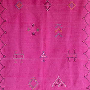 Close-up of a vibrant pink Moroccan rug featuring multicolored Berber symbols and geometric patterns, with a detailed handwoven texture