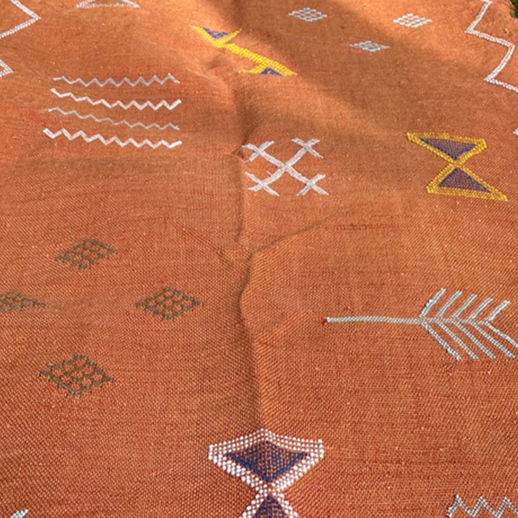 Close-up of a handwoven terracotta Moroccan runner rug with intricate Berber symbols and arrow motifs in white, yellow, and blue on grass